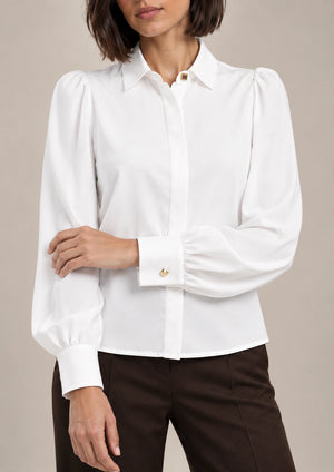 Detail of the white Serena shirt showing gathered puff sleeves, a wide cuff with a gold-tone button and a concealed front placket.
