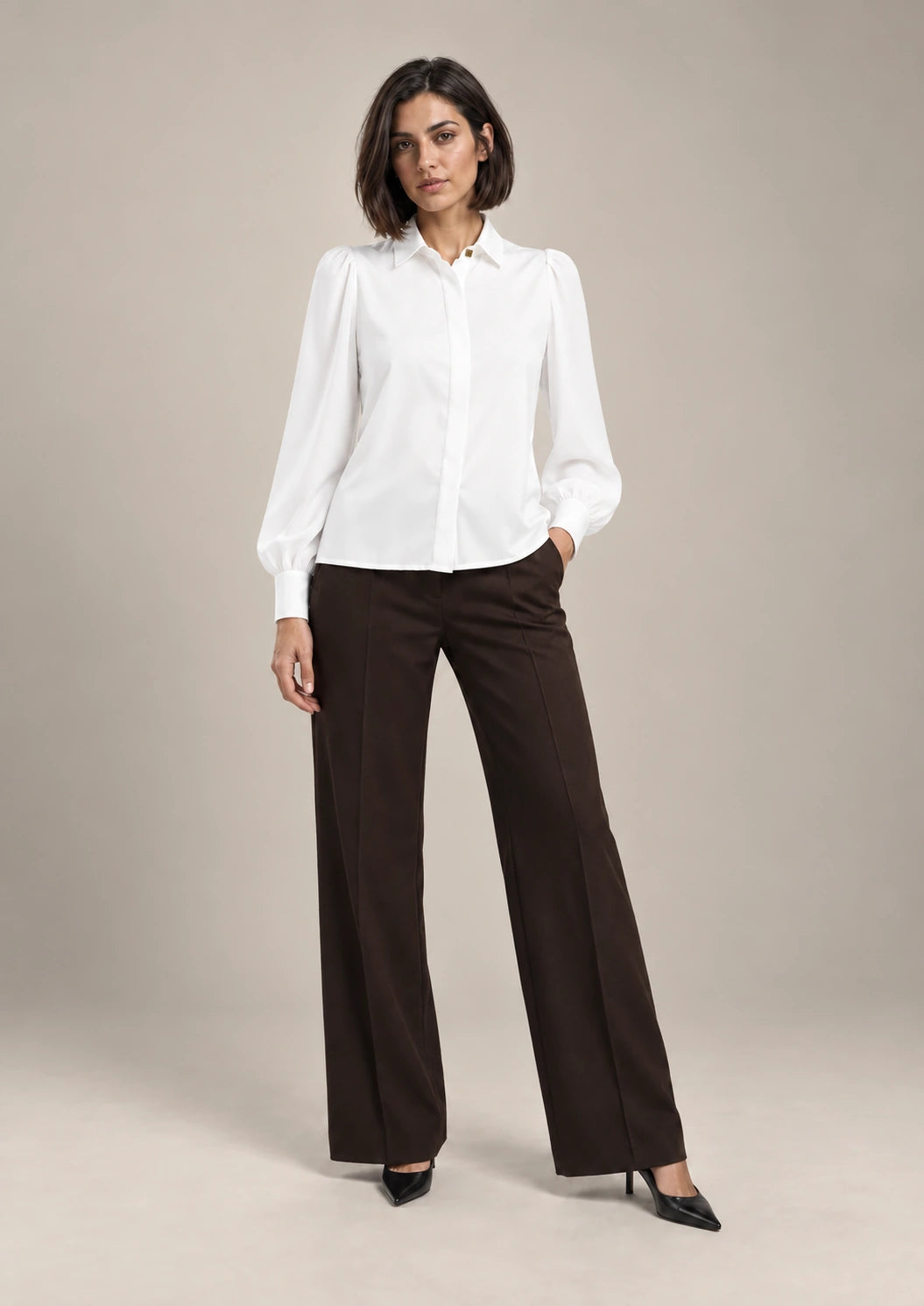Full-length styling view of the white Serena shirt with a pointed collar and long puff sleeves, worn with brown wide-leg trousers.