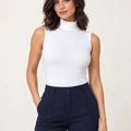 White stretch-cotton sleeveless mock-neck top styled with navy trousers, front view
